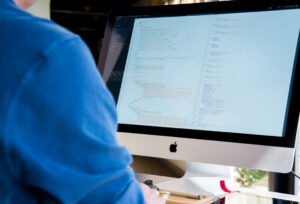 Person coding on an Apple iMac, displaying website maintenance code, relevant to WordPress support services.