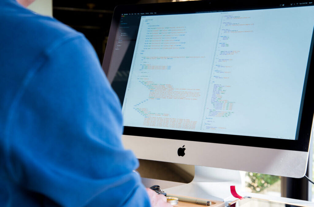 Person working on an Apple computer displaying code, representing website maintenance and WordPress support services.