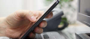 Hand holding a smartphone, with a computer and office setting in the background, emphasizing the call to schedule a consultation with WordPress experts.